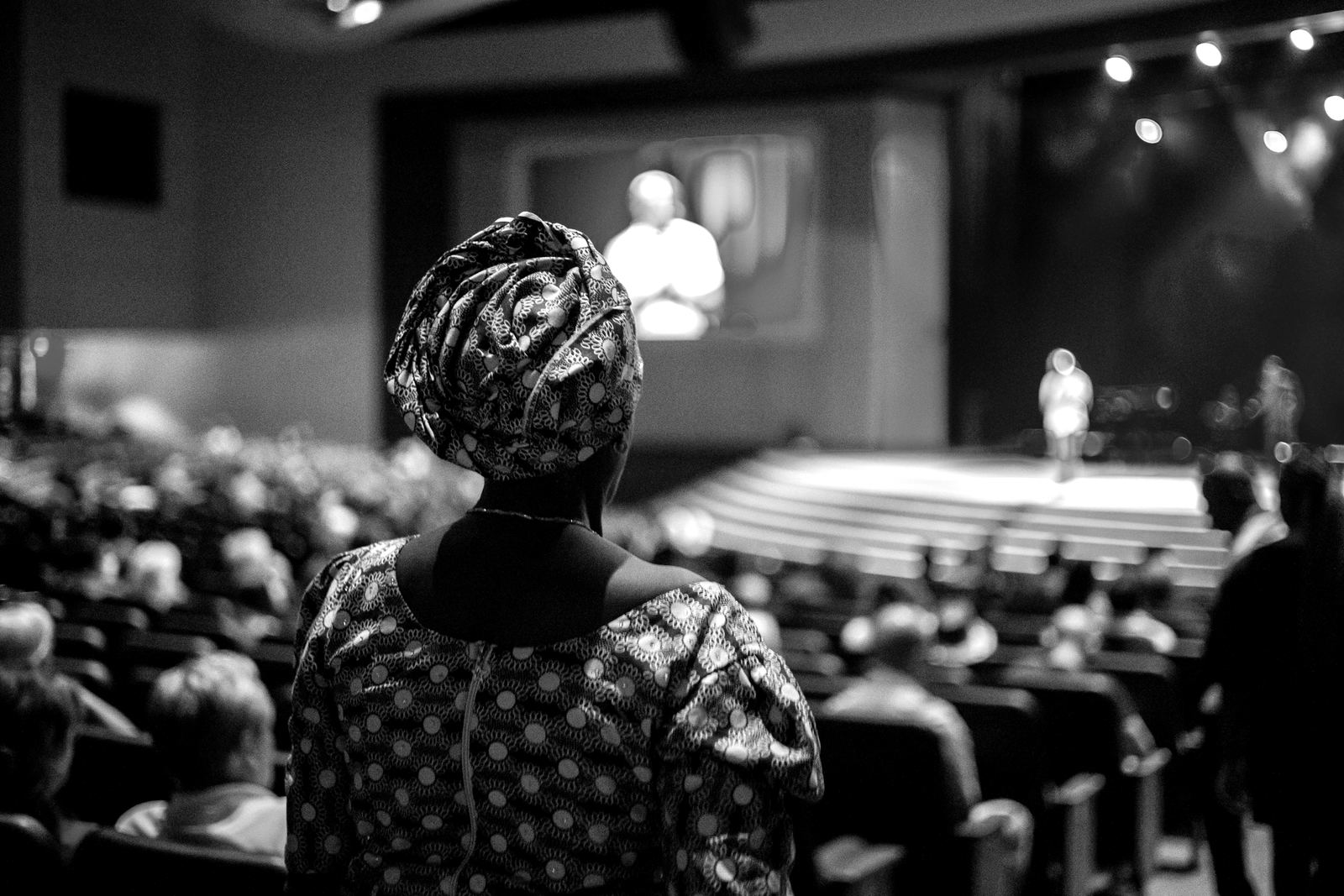 A delegate watching a speaker on stage in a large conference hall